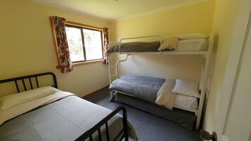 Une chambre avec deux lits superposés, un lit simple, une fenêtre avec des rideaux et un ventilateur de plafond.