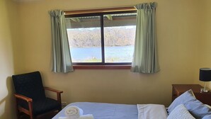 A hotel room with a bed, a chair, a window with curtains, and a lamp on a bedside table. - Lake Yalleena Nature Retreat (Lake Leake)