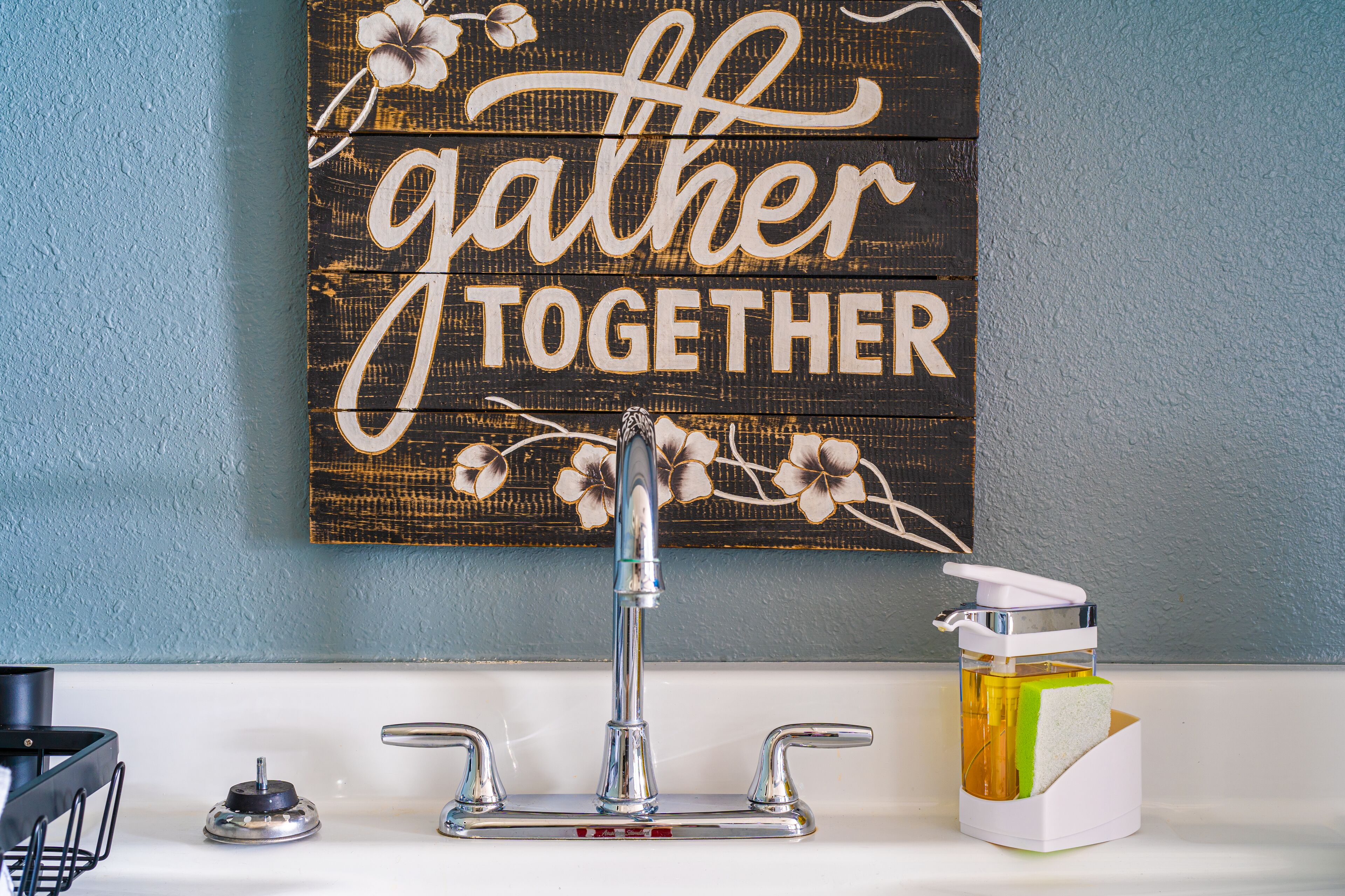 A bathroom with a wooden sign saying "Gather Together" above a sink.