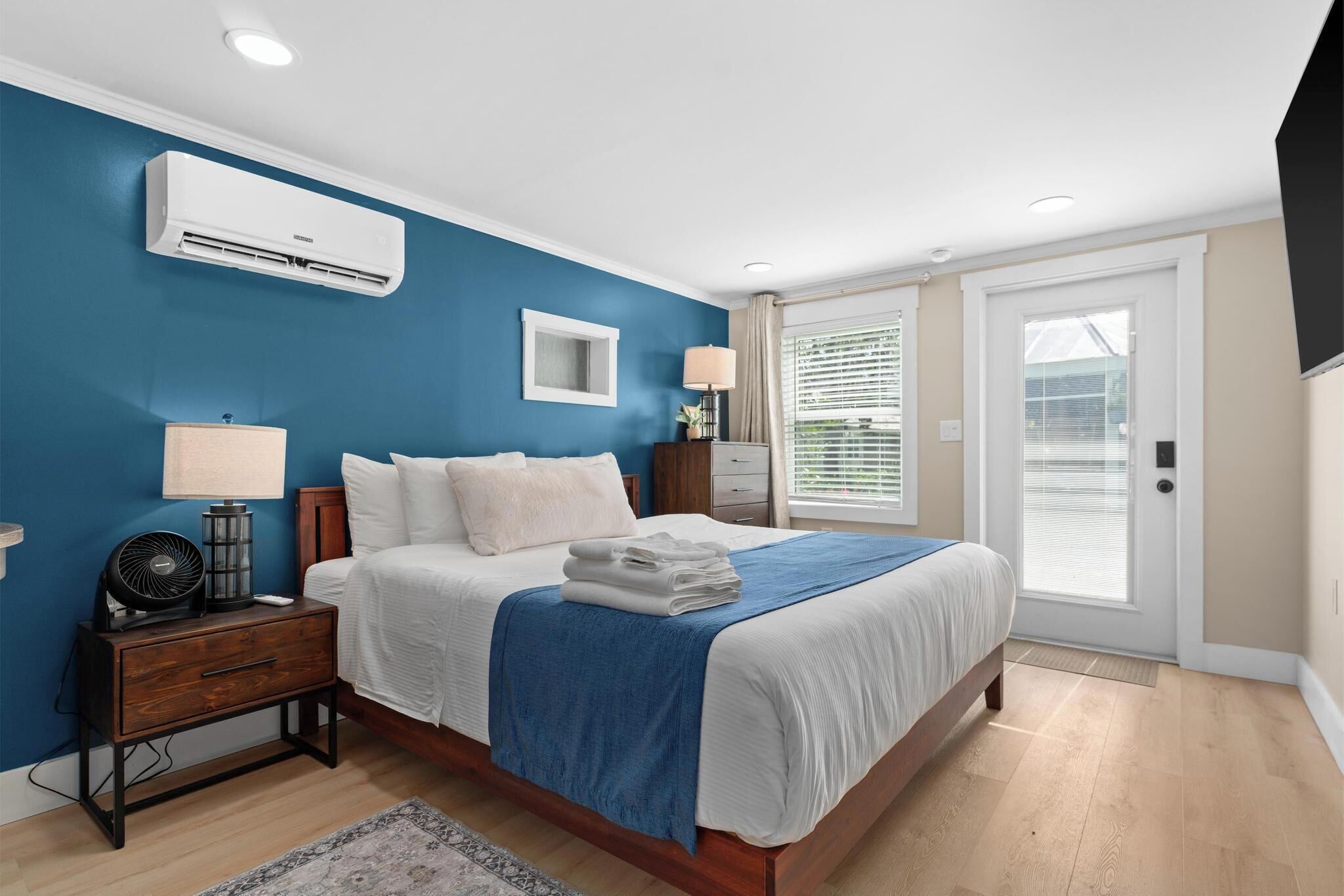 Un dormitorio con cama, mesitas de noche, lámpara, aire acondicionado y ventana con persianas.