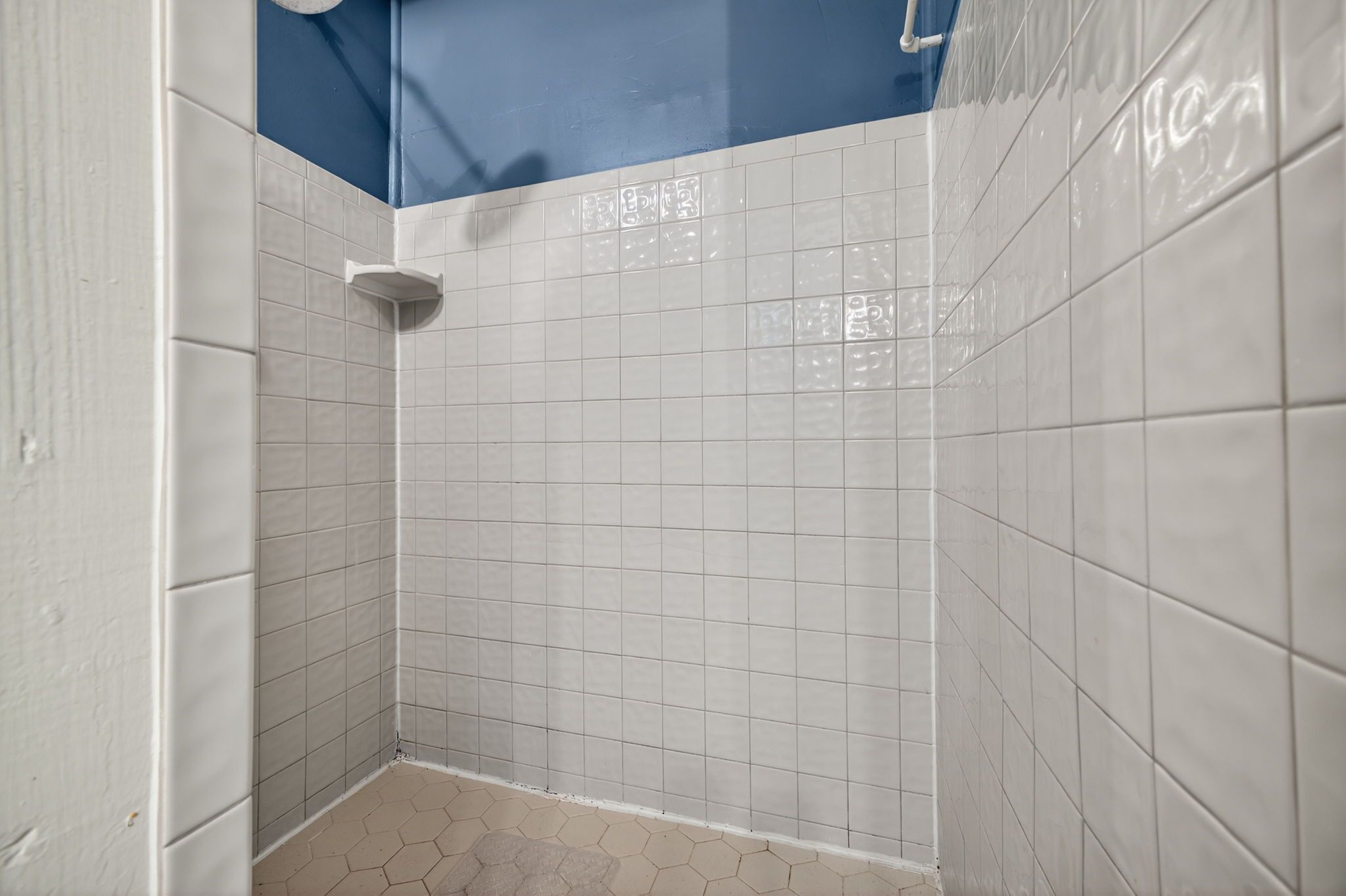 A corner of a bathroom with white tiled walls and a blue ceiling.