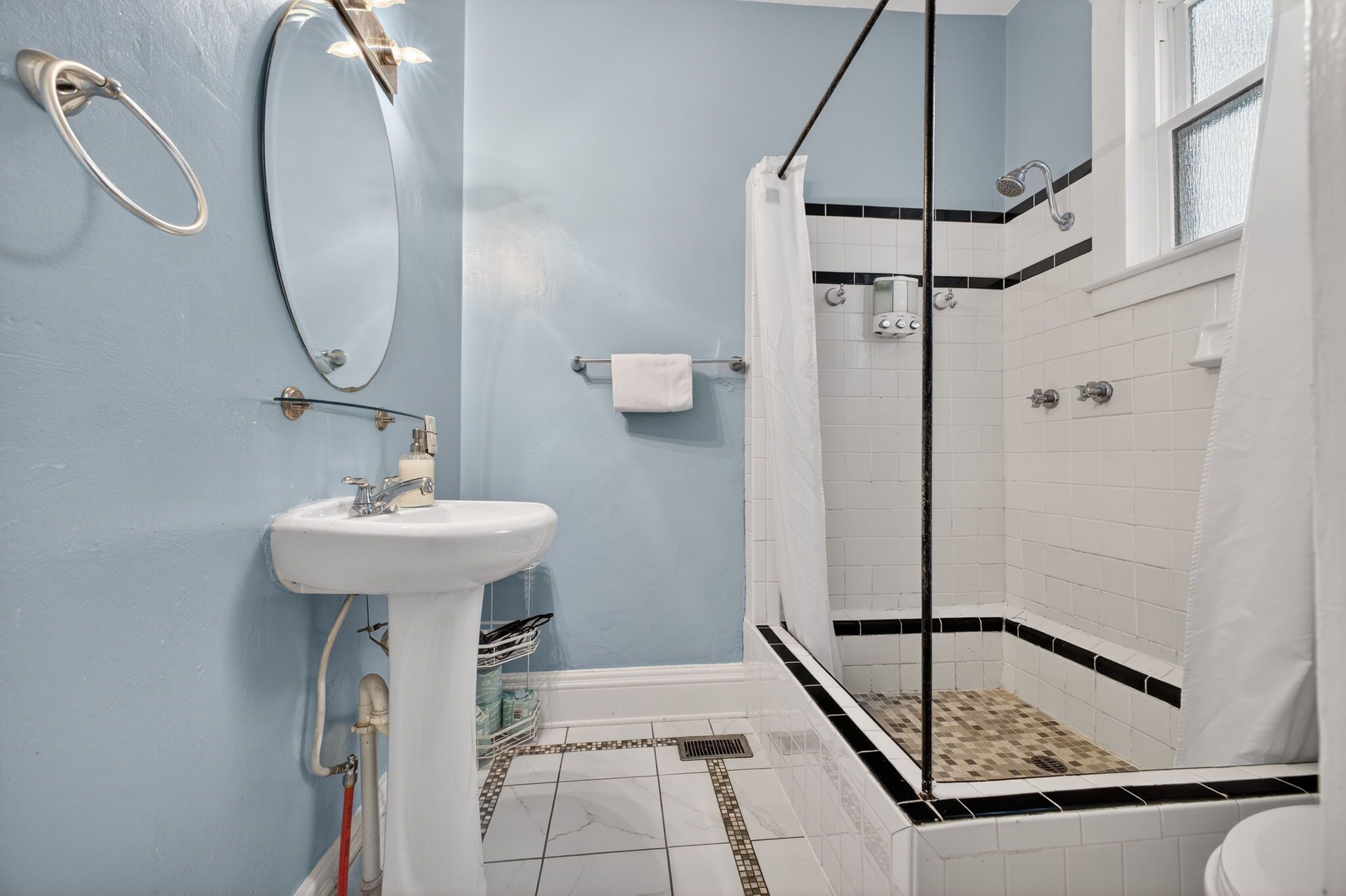 A bathroom with a sink, mirror, shower, and tiled walls.