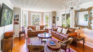 A spacious living room with two brown leather sofas, a coffee table, and a chandelier. There are bookshelves and a large mirror on the walls. - The Estate at Mount Dora (Mount Dora)