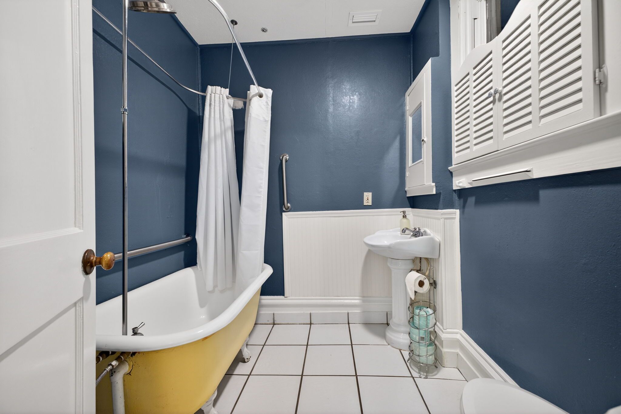 A bathroom with a yellow bathtub, white sink, and blue walls.