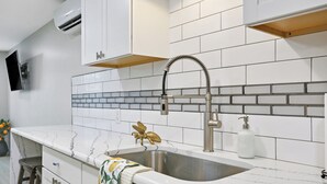 A kitchen with white cabinets, a stainless steel sink, and a backsplash with white and gray tiles. - The Estate at Mount Dora (Mount Dora)
