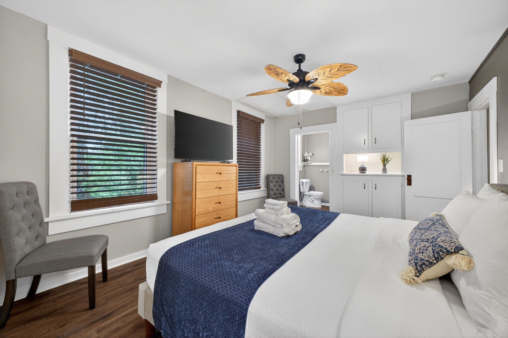 A bedroom with a bed, a television, a ceiling fan, a dresser, and a chair.