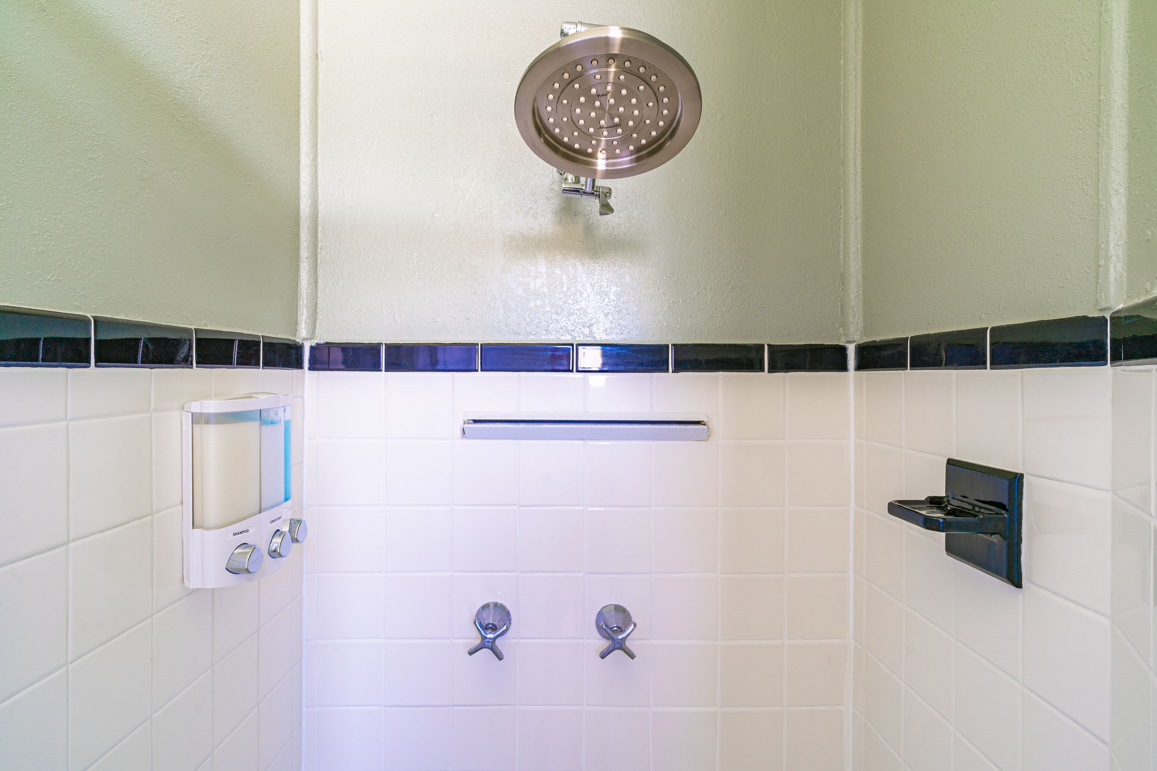 Un bagno con piastrelle bianche, una doccetta, un dispenser di sapone e un portasciugamani.
