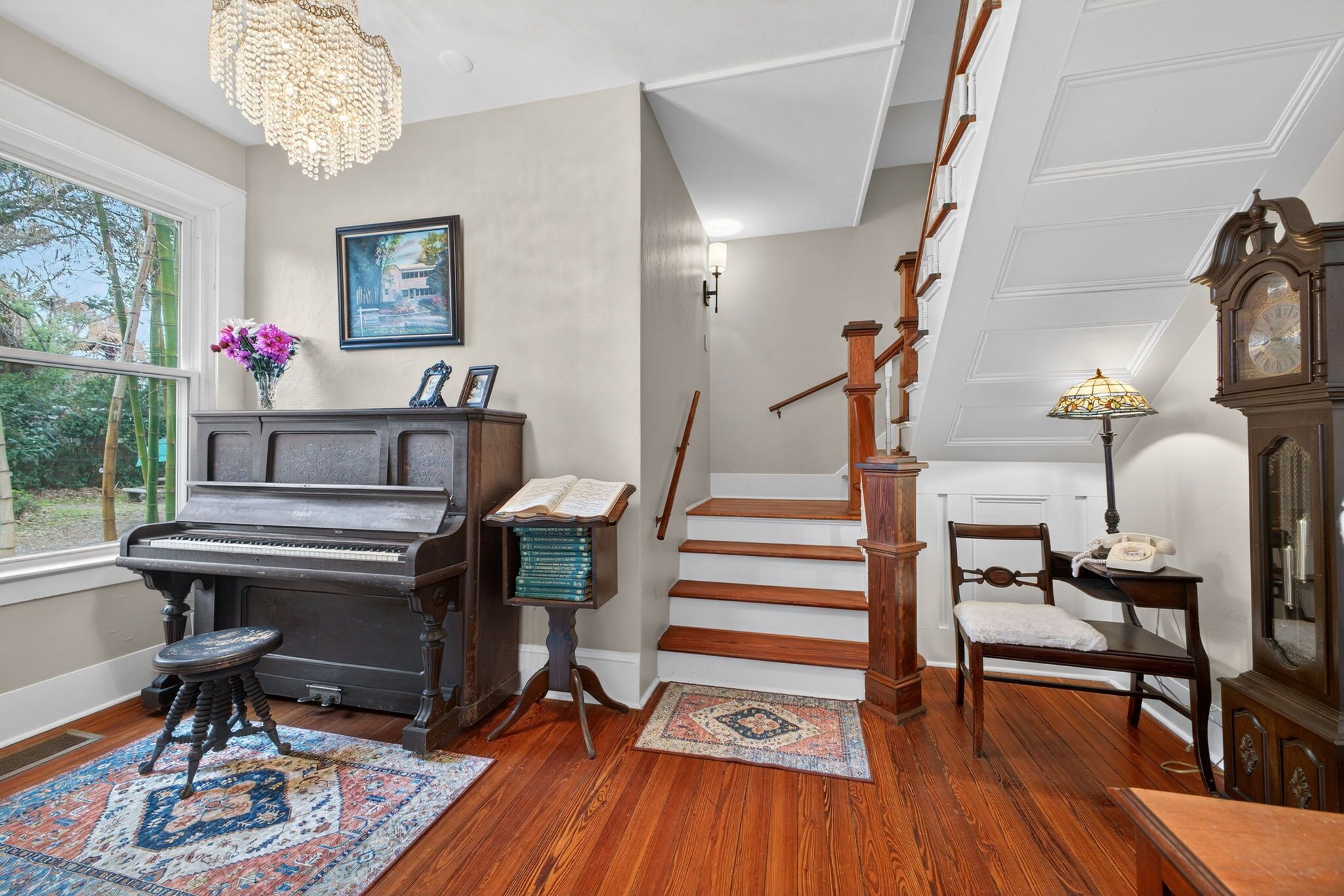 Una habitación con un piano, una escalera, una silla, una lámpara y un reloj.