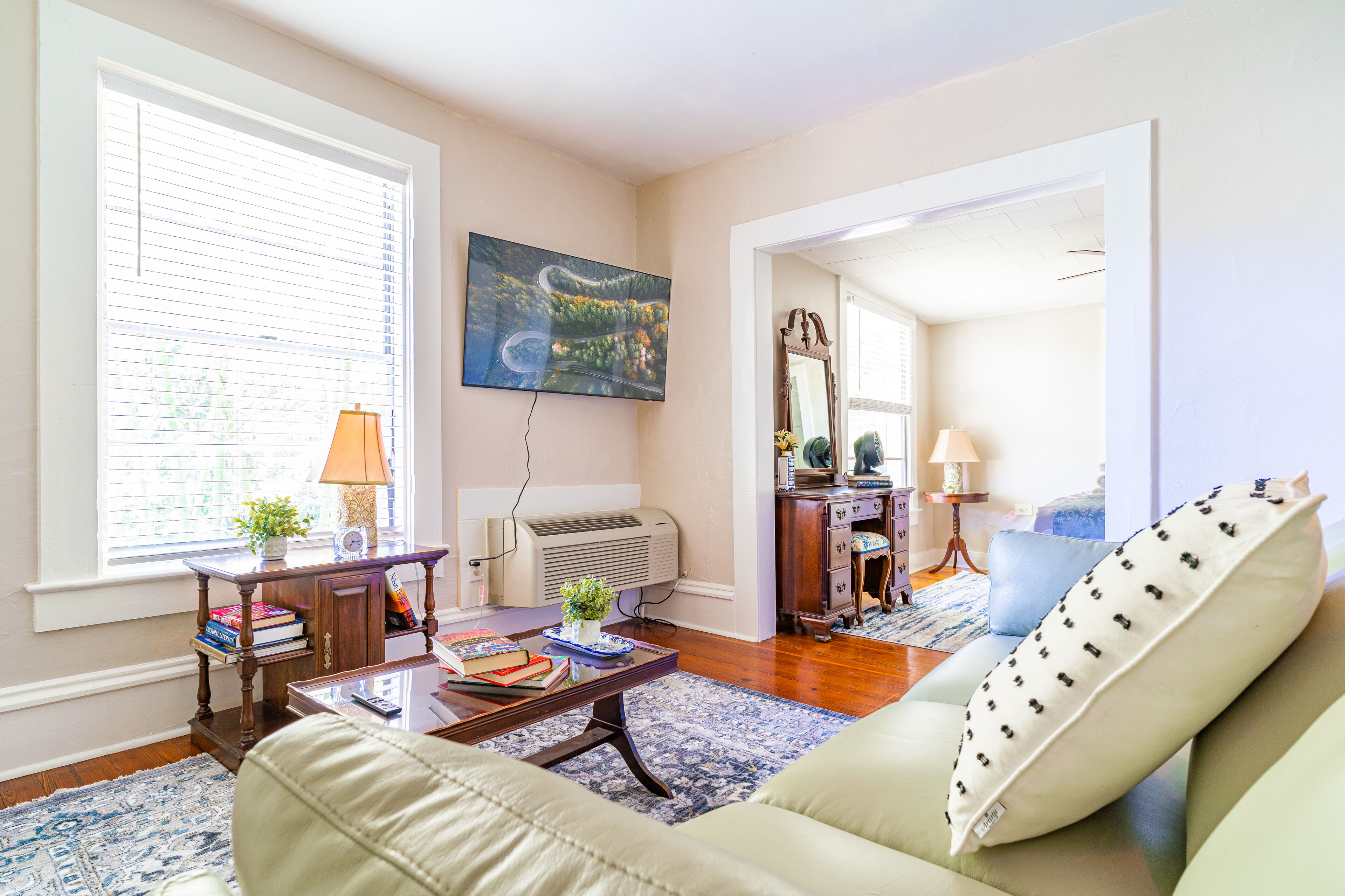 A living room with a sofa, a coffee table, a lamp, a painting, and a window with blinds.
