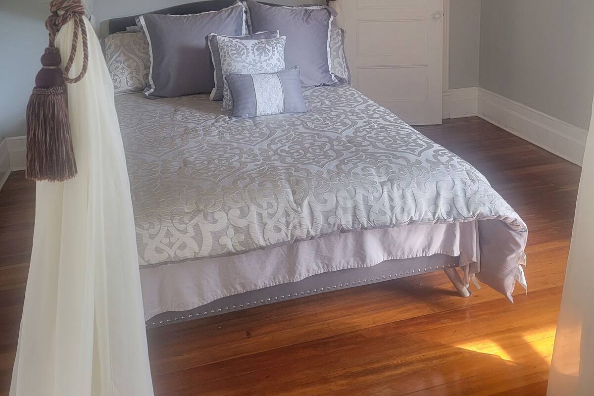 A bedroom with a large bed, a chandelier, a mirror, and a door.