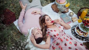 Una pareja acostada sobre una manta al aire libre, con una preparación para picnic que incluye pastel, frutas y bebidas.