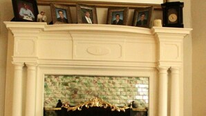 Una chimenea con repisa que exhibe fotos enmarcadas, un reloj y un revoque de azulejos.