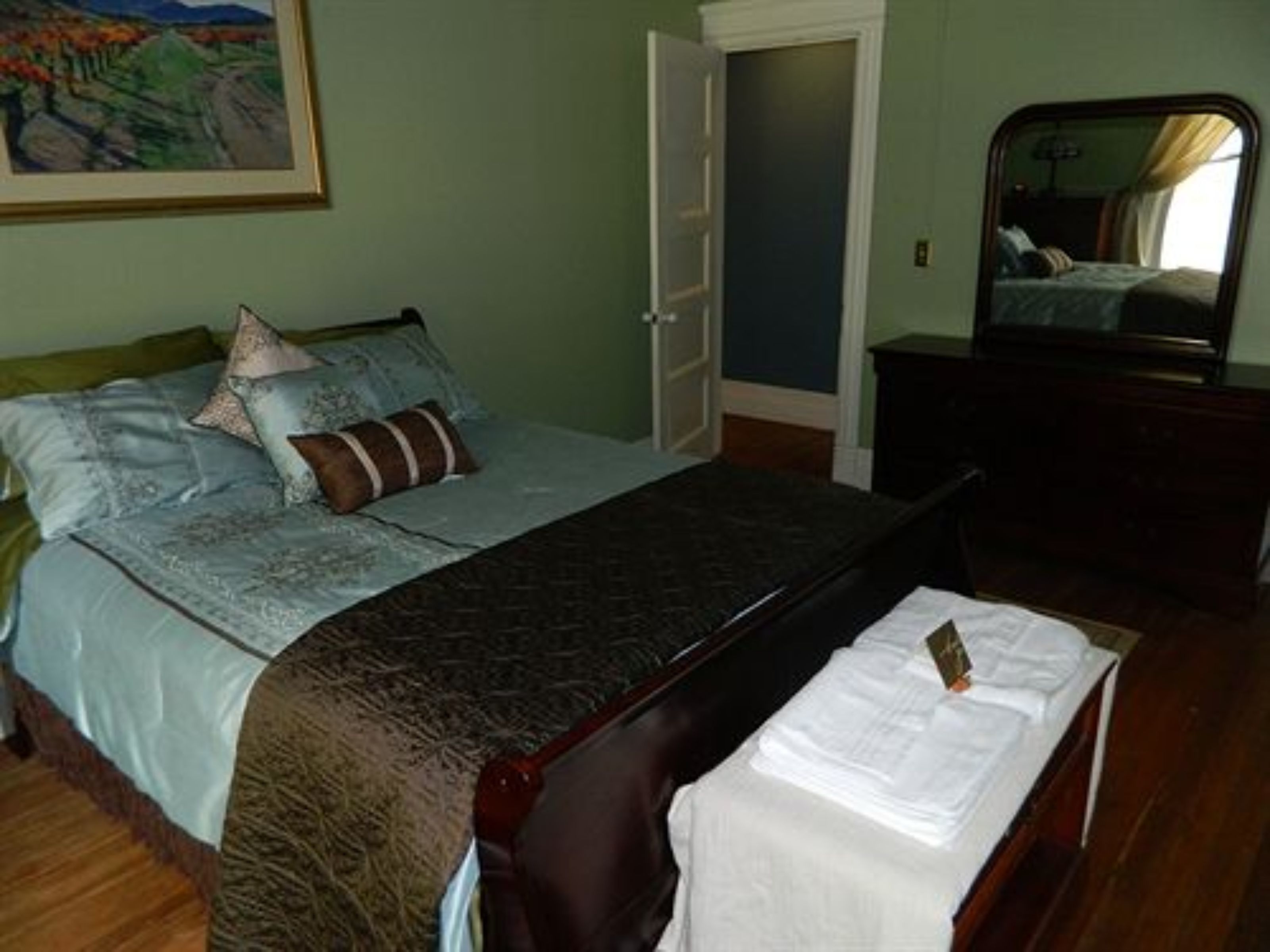 A bedroom with a bed, a dresser, a mirror, and a painting on the wall.