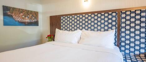 Una habitación de hotel con una cama grande, un cabecero estampado, un cuadro en la pared y un jarrón con flores.
