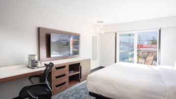 Quarto de hotel com cama, escrivaninha com computador, cadeira, televisão e varanda com vista para o exterior.