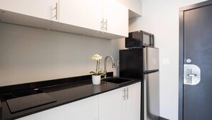A modern kitchen with white cabinets, a black countertop, a built-in microwave, and a refrigerator.