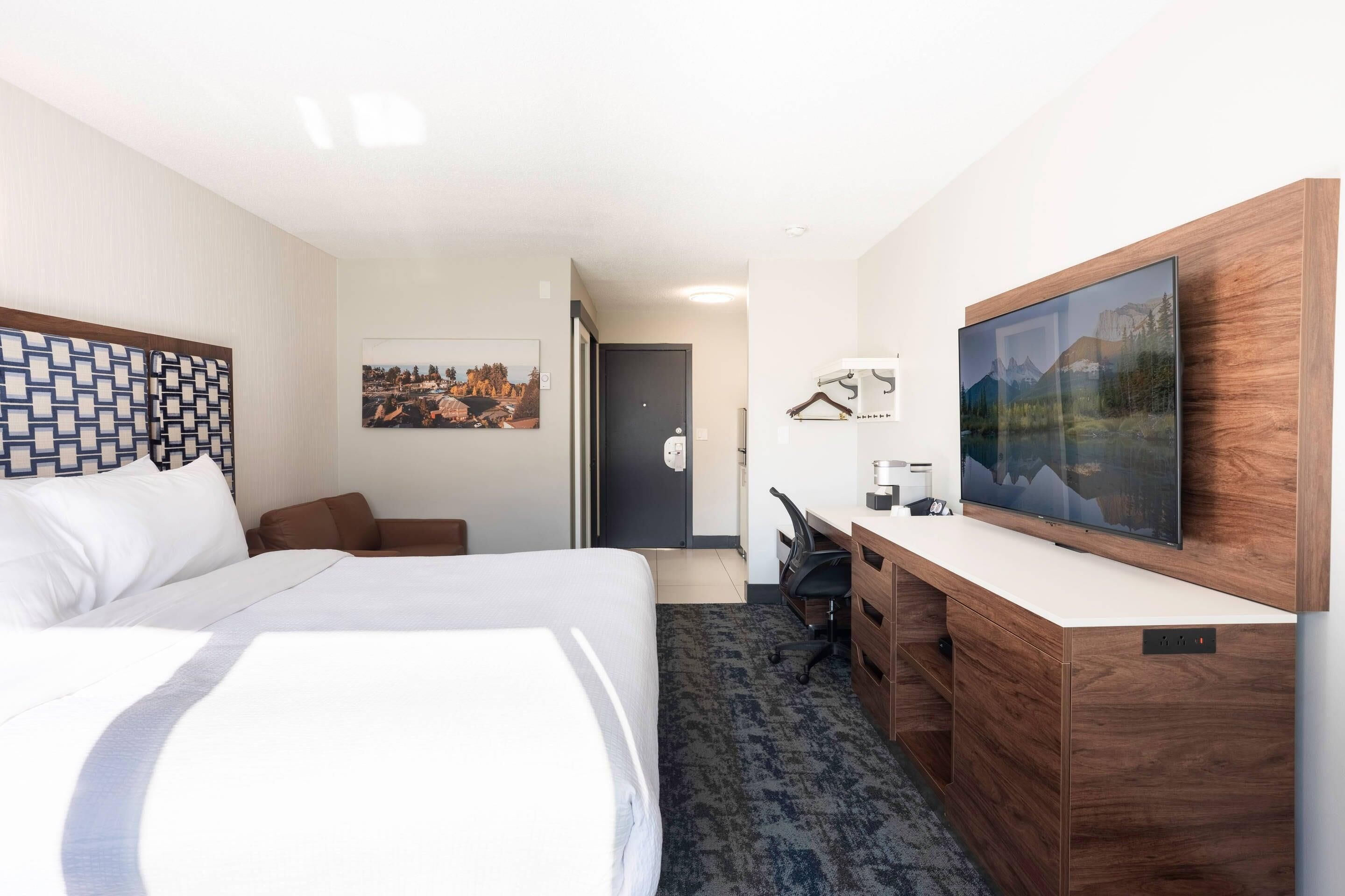 Habitación de hotel con cama, escritorio, silla, televisión y puerta que da a otra habitación.