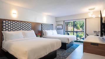 A hotel room with two beds, a desk, and a large window with a view of greenery.