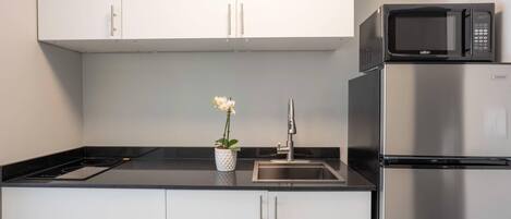 Una cocina moderna con armarios blancos, un refrigerador de acero inoxidable, un microondas y un lavamanos.
