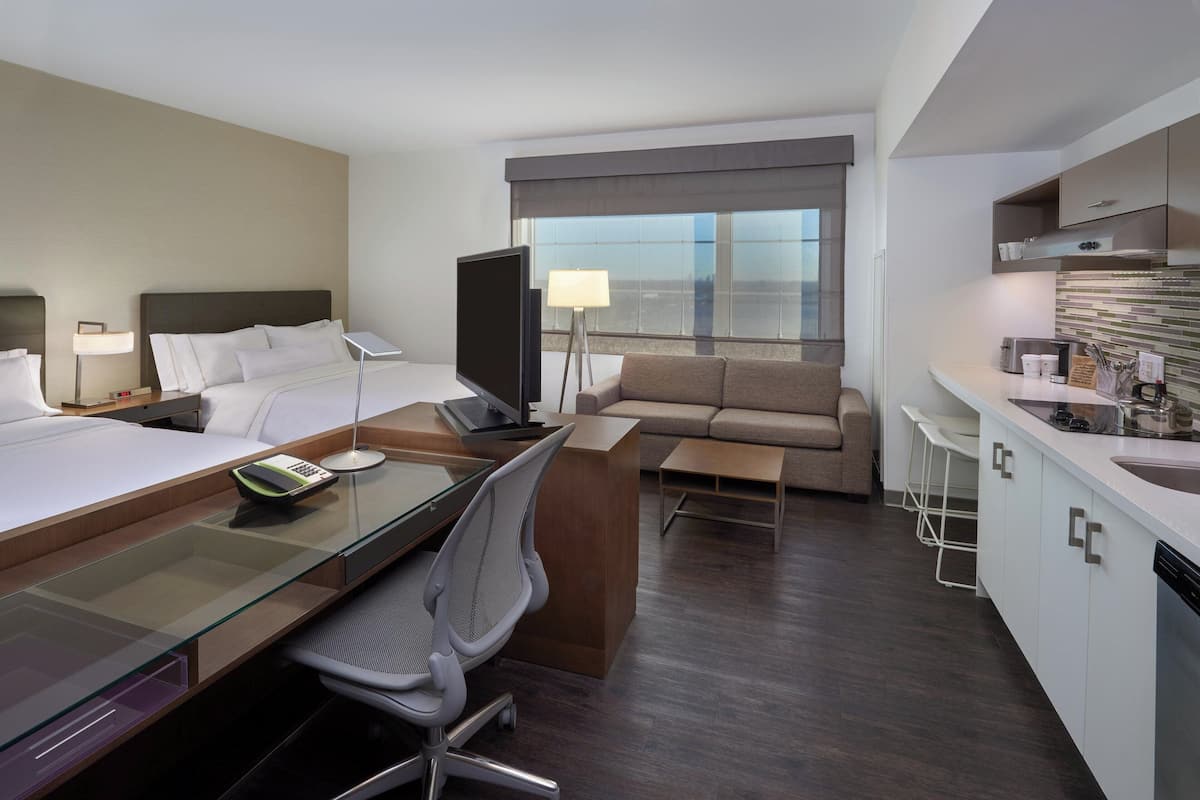 Una habitación de hotel con cama, escritorio, silla, televisor, sofá y kitchenette.