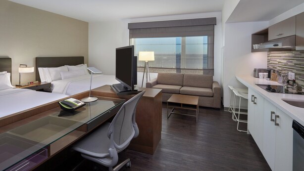 A hotel room with a bed, desk, chair, TV, sofa, and kitchenette.