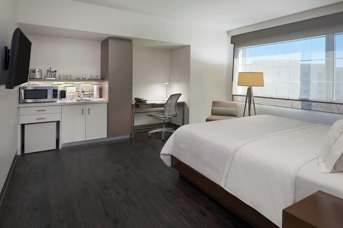 Habitación de hotel con cama, escritorio, silla, microondas, cafetera y televisión.