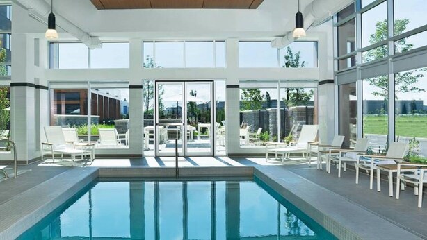 A modern indoor pool area with clear glass walls, a pool, and lounge chairs.