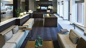 A spacious hotel lobby with a central seating area, a reception desk, and large windows providing natural light.