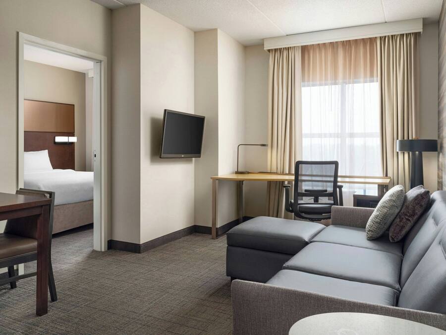 A hotel room with a bed, a desk with a chair, a sofa, a TV, and a window with curtains.