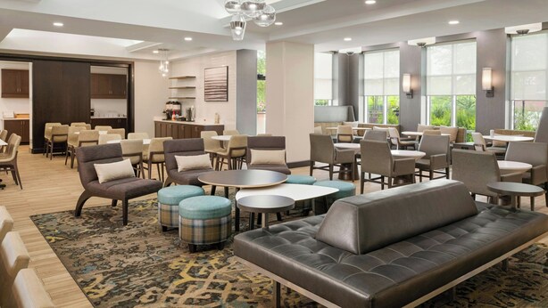 A modern hotel lobby with a seating area featuring sofas and chairs, a coffee station, and large windows offering a view of greenery. - Residence Inn by Marriott Ottawa Airport (Ottawa)