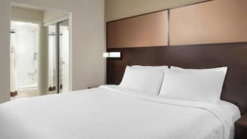 A large bed with white linens, a dark headboard, and a nightstand with a lamp.