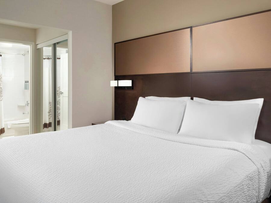 A large bed with white linens, a dark headboard, and a nightstand with a lamp.