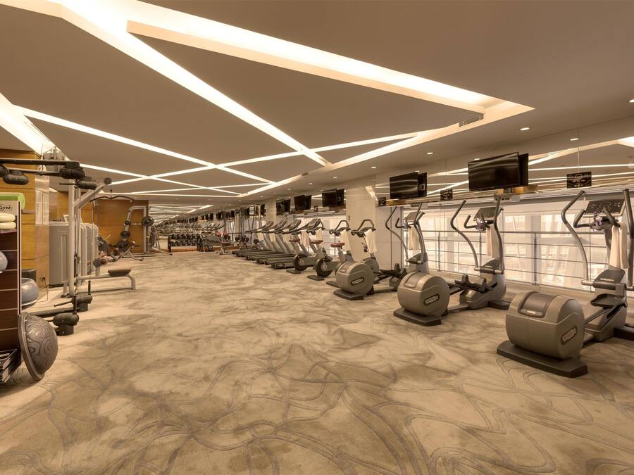 A modern gym with various cardio machines, weightlifting equipment, and a patterned floor.