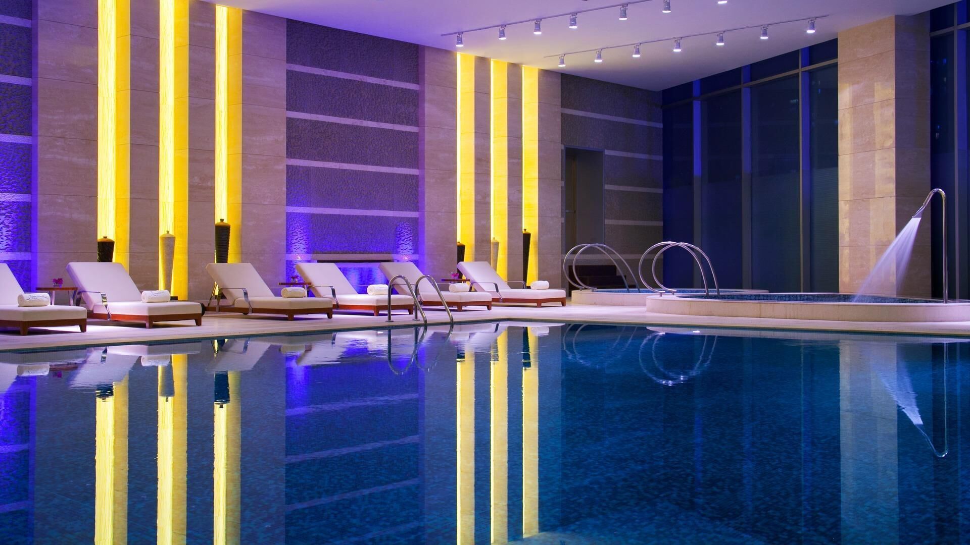 A modern indoor swimming pool with lounge chairs and a clear pool.