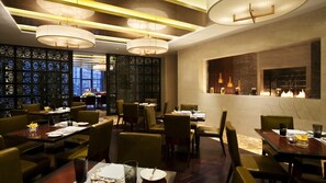 A restaurant with multiple tables and chairs, a decorative wall with intricate patterns, and a modern chandelier. - Kempinski Hotel Taiyuan (Taiyuan)