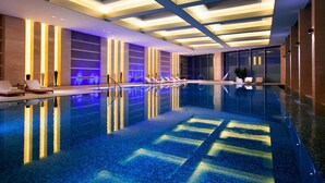 Ein moderner Innenpool mit klarem Wasser, versenkten Liegen und einer Decke mit geometrischer Beleuchtung.