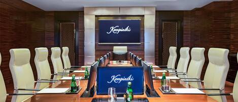 A conference room with a long table, white chairs, and a large screen displaying "Kempinski".