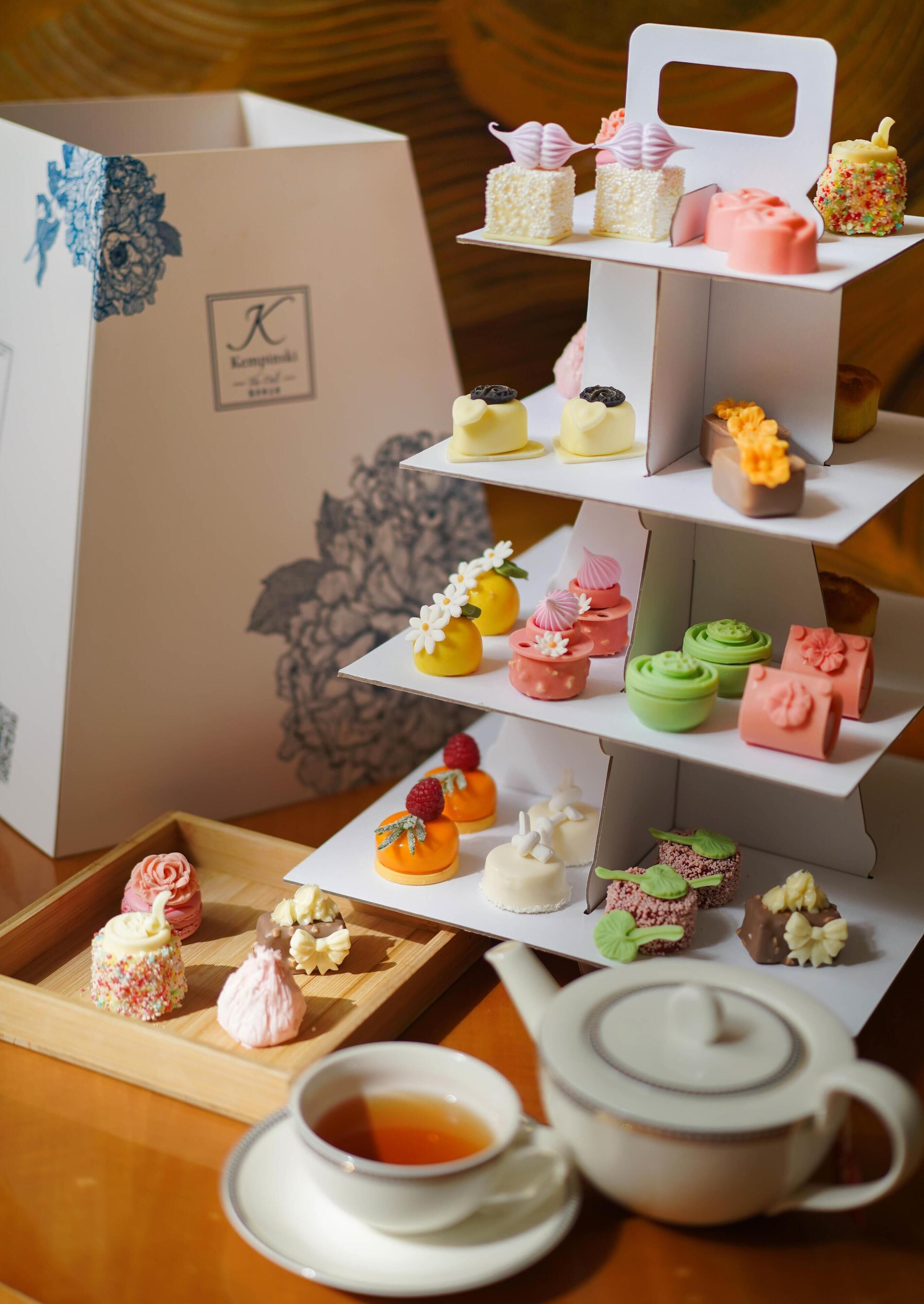 A tiered dessert display with various pastries and a teapot with a cup of tea on a wooden table.