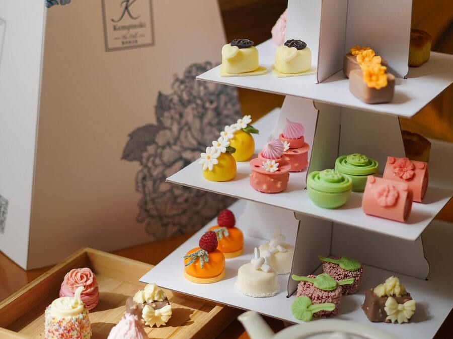 A tiered dessert display with various pastries and a teapot with a cup of tea on a wooden table.