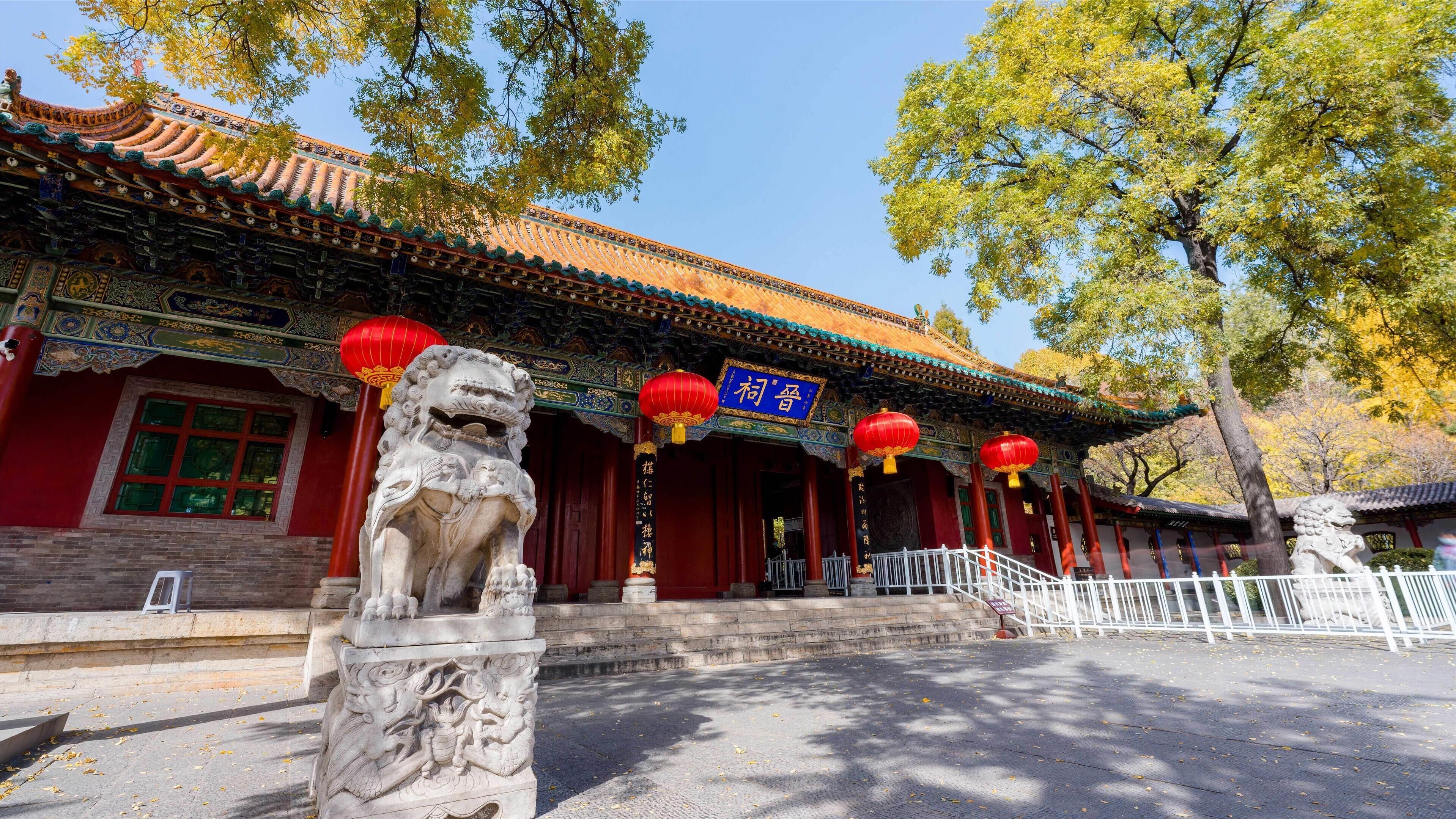 Un edificio chino tradicional con arquitectura ornamentada, una estatua de león y faroles rojos.
