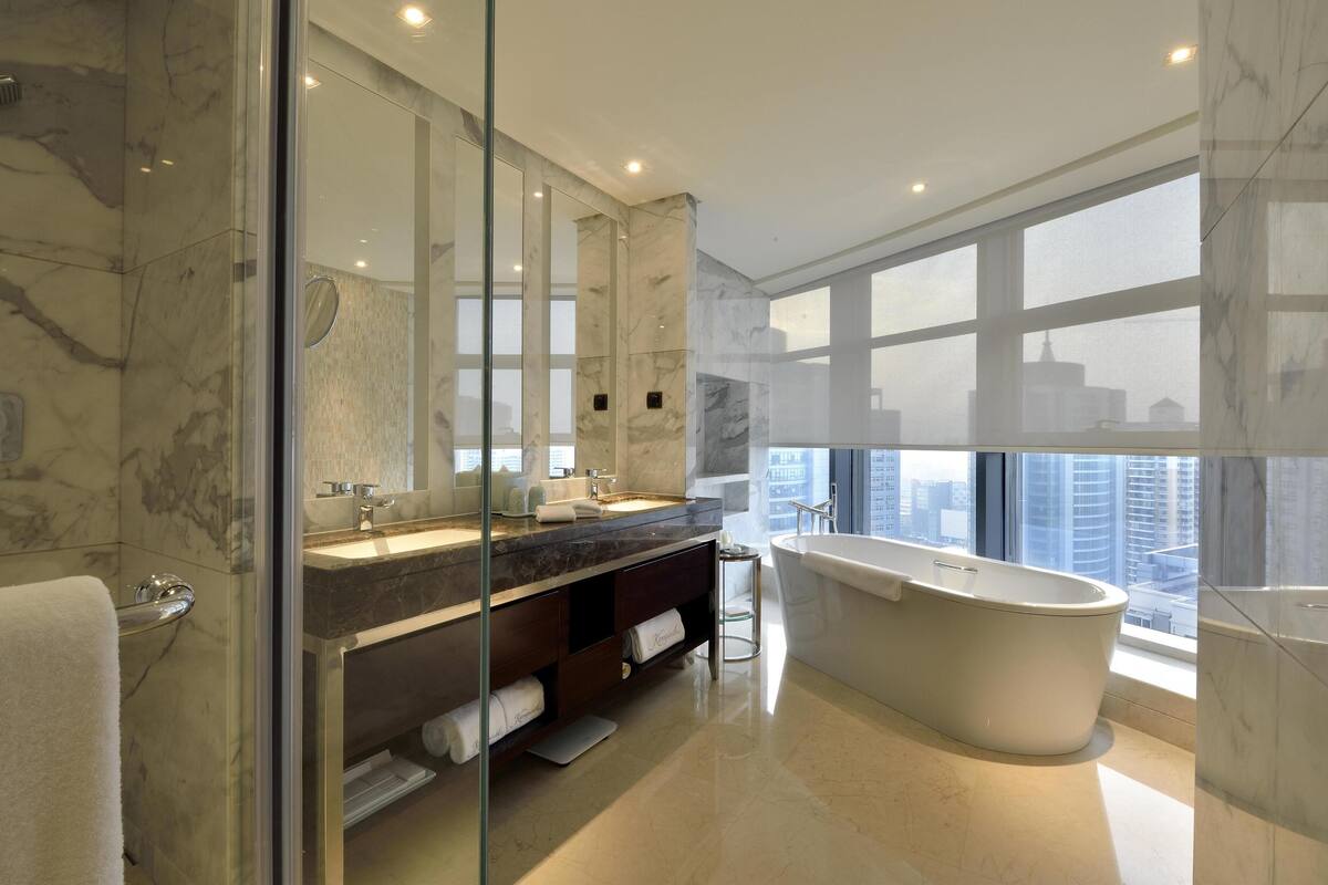 Une salle de bain moderne dotée d’une grande baignoire, d’une douche à parois de verre et d’un meuble-lavabo avec un plan de travail en marbre.