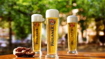 Three glasses of beer with the label "PAULANER" on a wooden surface with a pretzel.