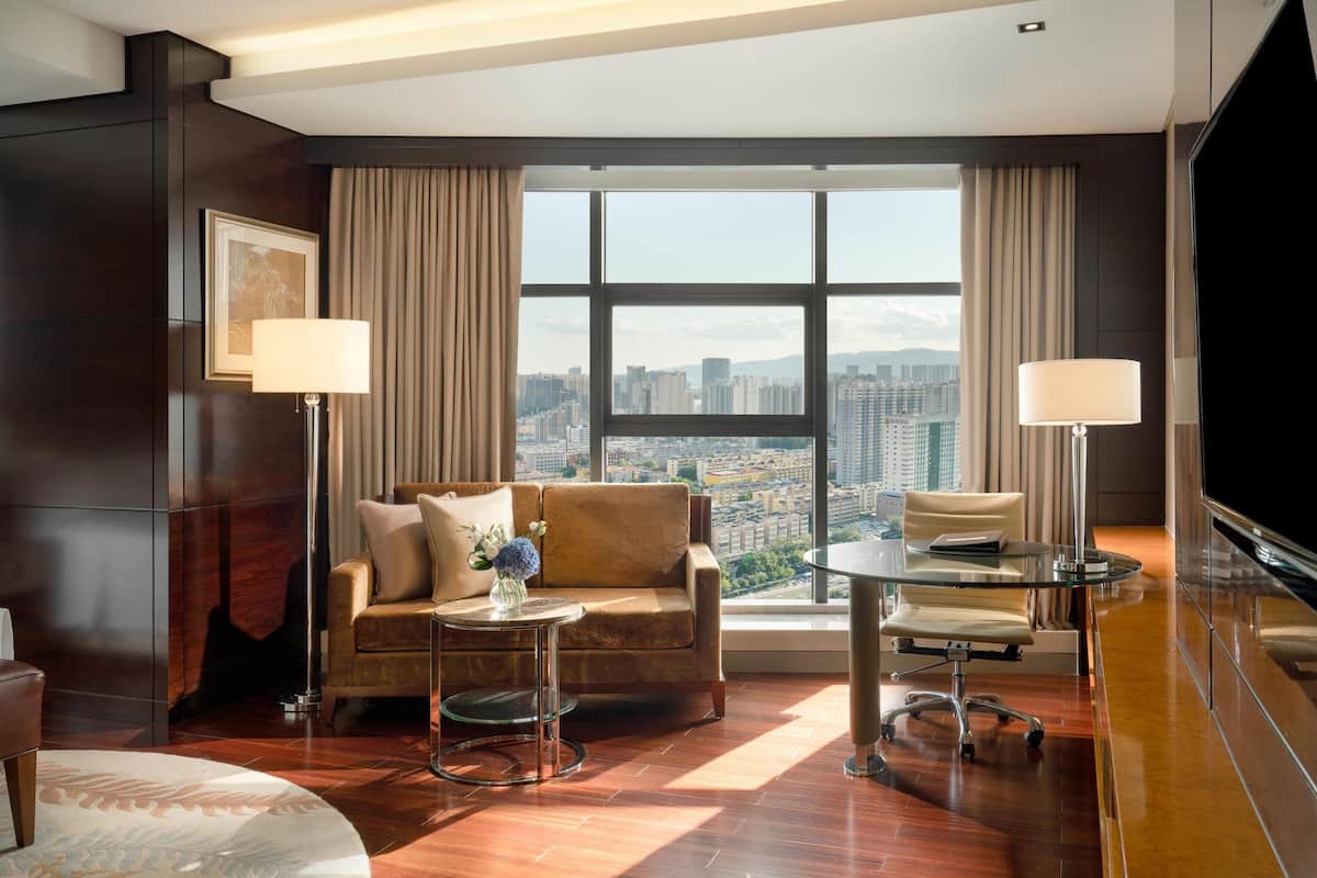 Une chambre d’hôtel moderne dotée d’une grande fenêtre donnant sur la ville, d’un canapé, d’une petite table et d’un téléviseur.