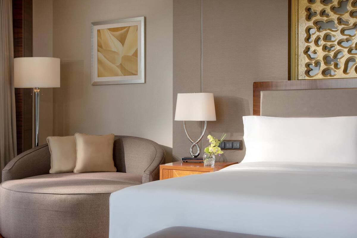 Une chambre d’hôtel comprenant un lit, deux tables de chevet, une lampe, une chaise et un élément décoratif mural.