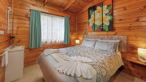 Une chambre à coucher dans une cabane en bois, avec un lit, une table de chevet, une lampe, un lavabo et une fenêtre avec des rideaux.