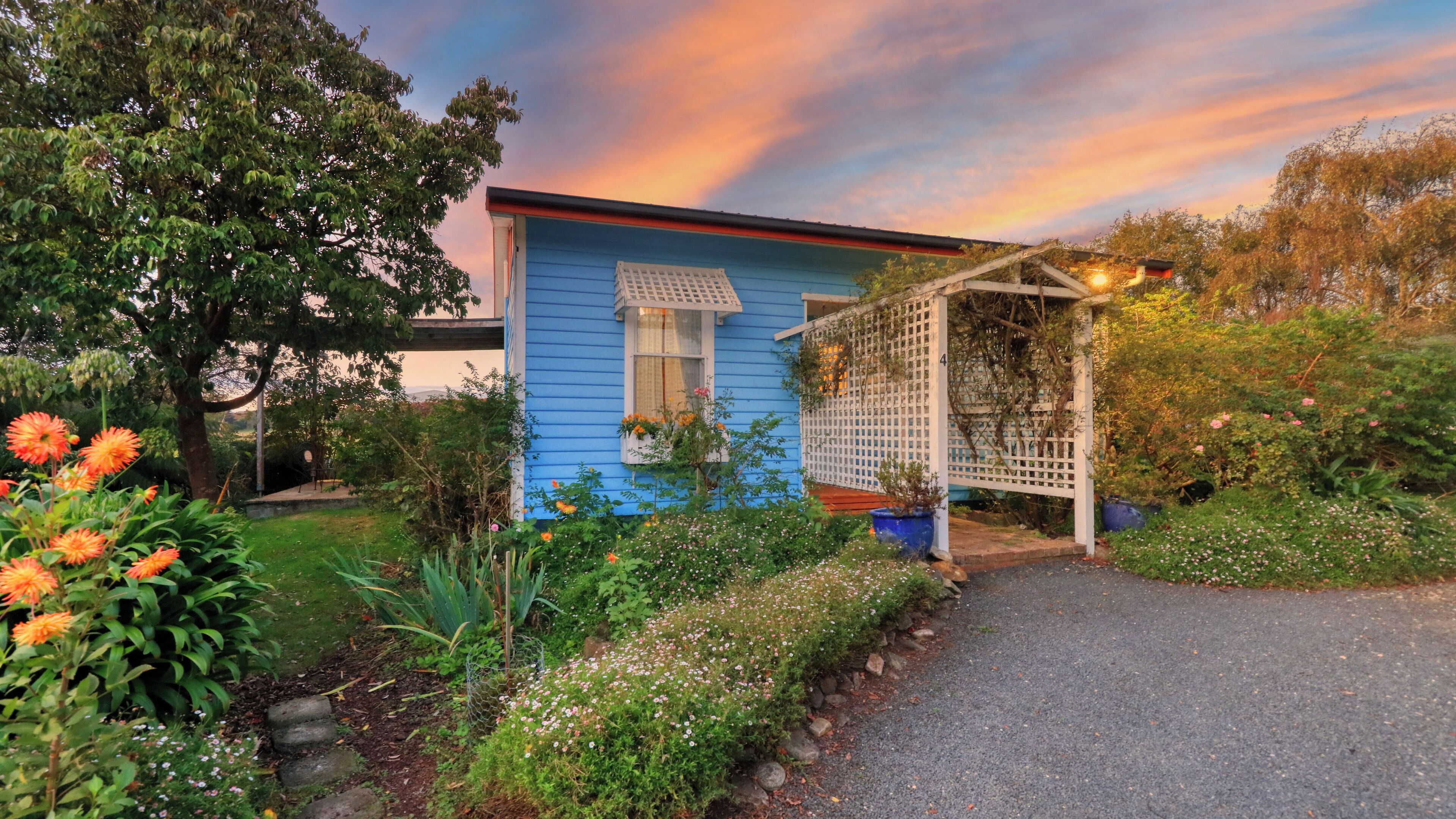A blue house with a garden, a pergola, and a pathway leading to the entrance.