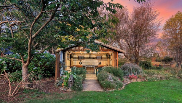 Un chalet rustique en bois, doté d’un porche, entouré d’une végétation luxuriante et de plantes en fleurs.