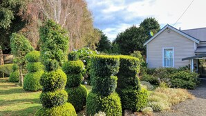 Un jardin bien entretenu, avec des haies taillées avec soin, et une maison dont la porte et les fenêtres sont bien visibles.