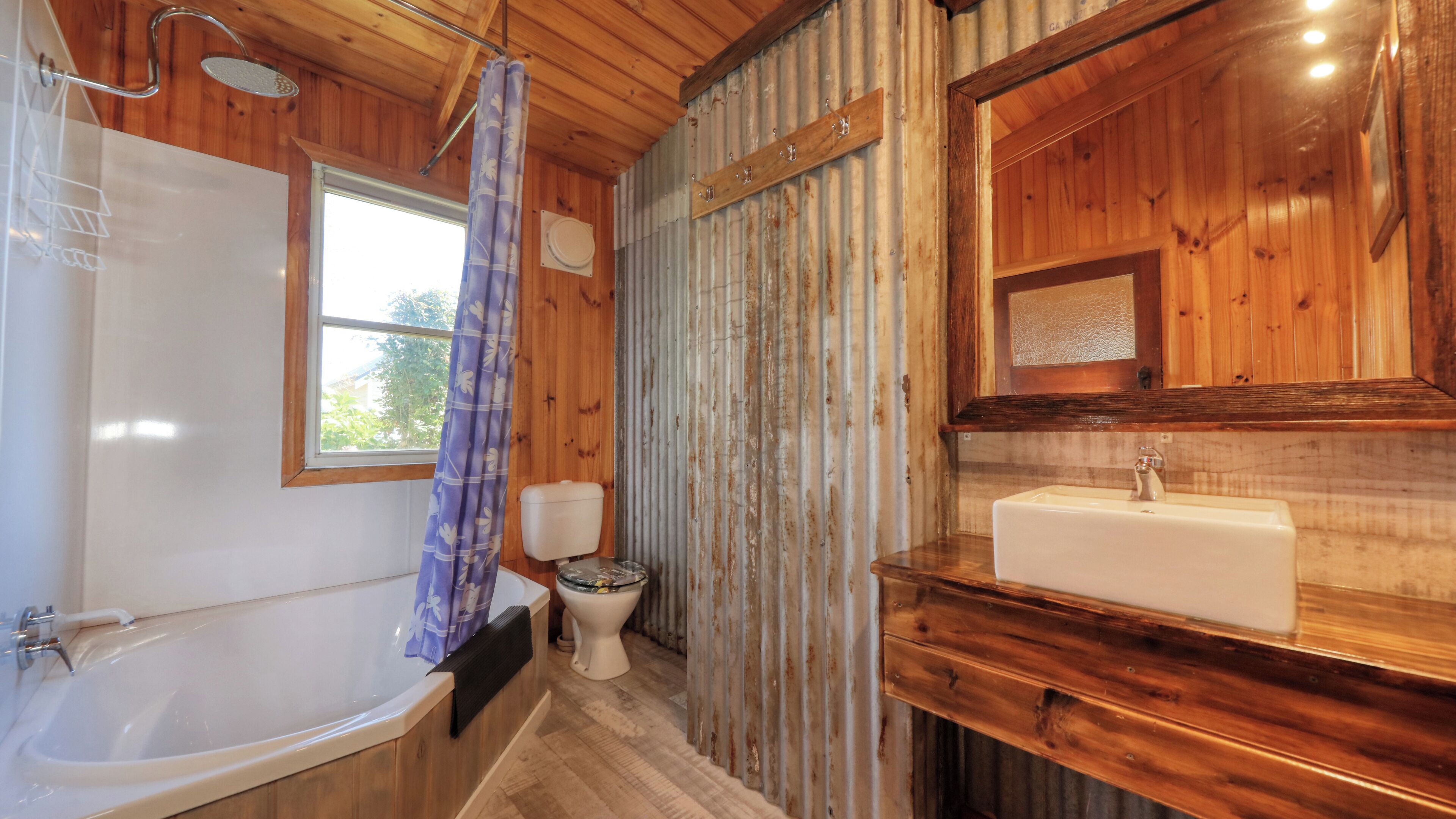Een badkamer met houten details, een bad, een toilet en een wastafel met spiegel erboven.
