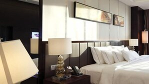 Quarto de hotel com uma cama grande, mesas de cabeceira, uma escrivaninha e uma cadeira.